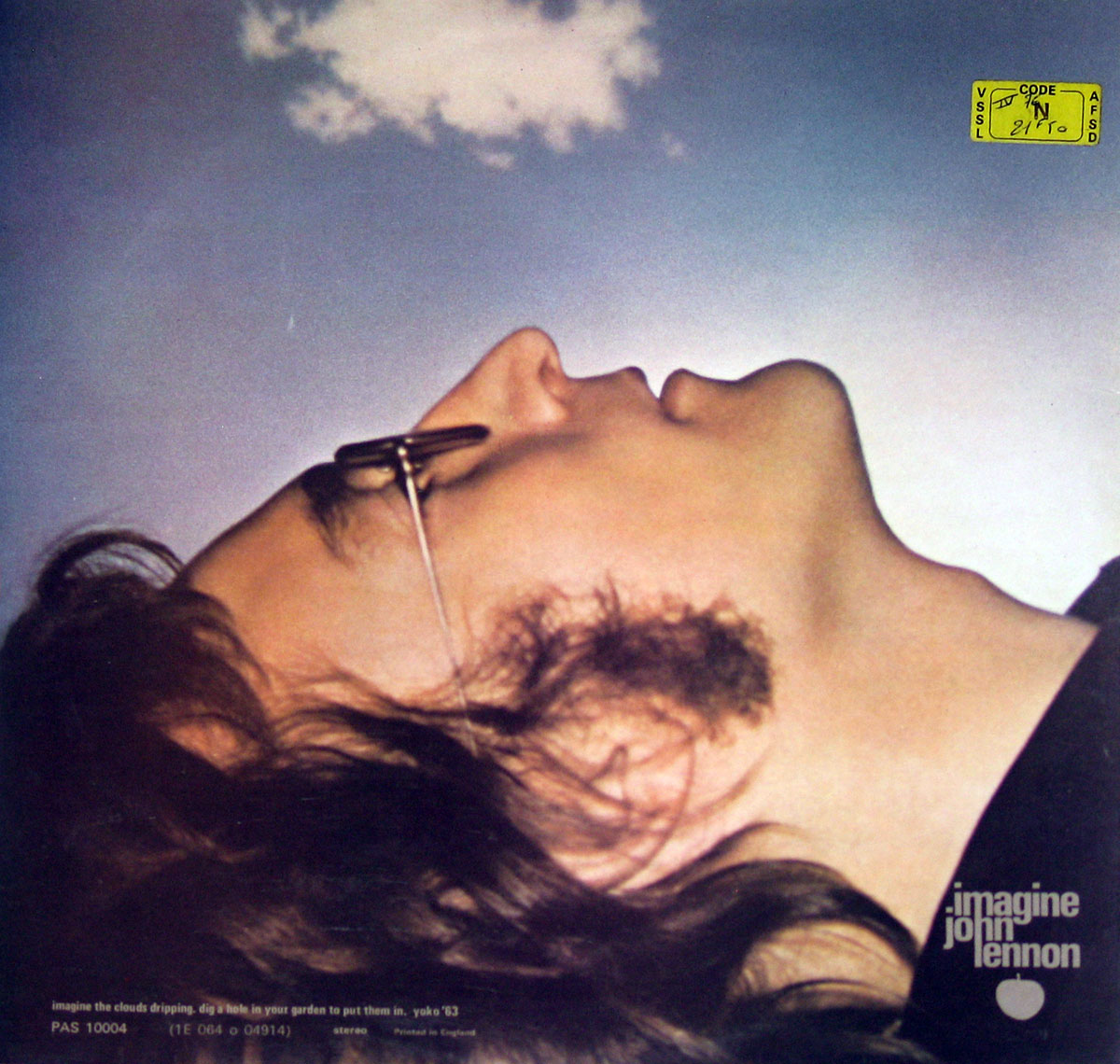 Back cover of John Lennon's 'Imagine' album, featuring a side-profile shot of Lennon lying down with his face turned upward toward a blue sky with a single white cloud.